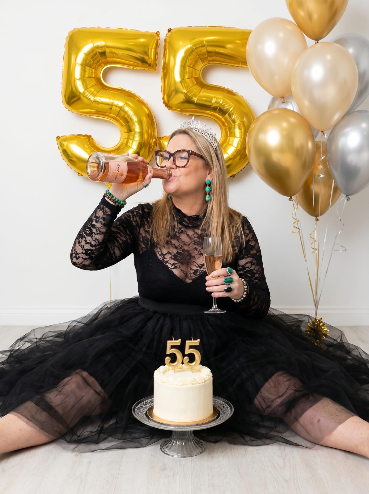 Gemma in a tiara swigging rosé in front of giant gold 55 balloons